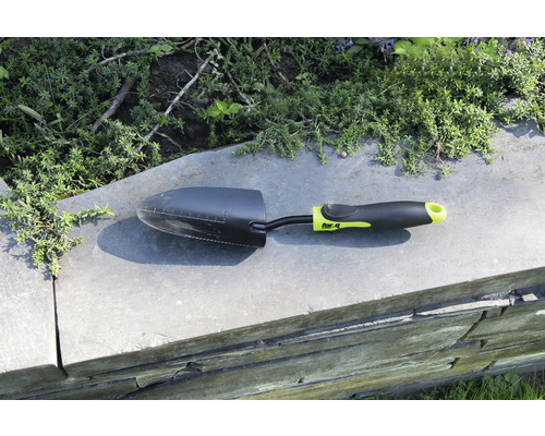 Záhradná lopatka na múre s rastlinami v pozadí