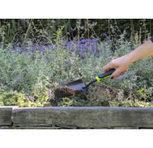 Osoba používa malú záhradnú lopatku na hrabanie v kvetinovom záhone.