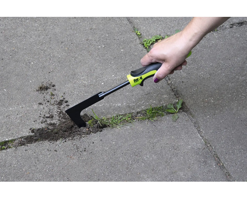 Ruka používa škrabku na škáry na odstraňovanie buriny medzi dlažobnými kameňmi.