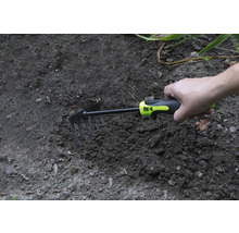 Ruka drží malú motyku v záhradnej pôde