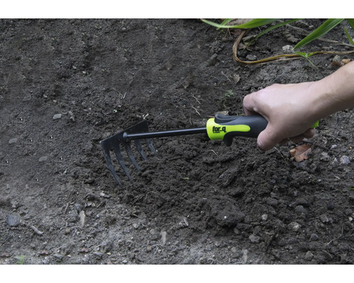 Ruka drží malú motyku v záhradnej pôde