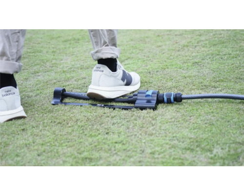 Záhradný zavlažovač na trávniku s nohou na porovnanie veľkosti.