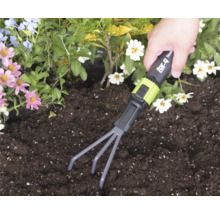 Ruka používa ručné hrabličky for_q v tmavej pôde v záhone s kvetmi.