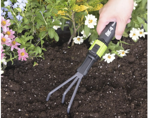 Ruka používa ručné hrabličky for_q v tmavej pôde v záhone s kvetmi.