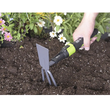 Ruka používa ručnú motyčku for_q so zubami a listom v tmavej pôde vedľa kvetov na kyprenie zeme.