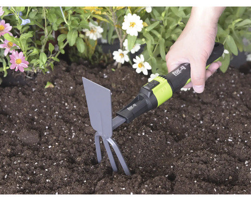 Ruka používa ručnú motyčku for_q so zubami a listom v tmavej pôde vedľa kvetov na kyprenie zeme.