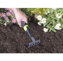 Ručné hrabličky s čierno-zelenou rukoväťou a for_q Logo používané v tmavej zemine medzi ružovými a bielymi kvetmi.