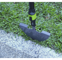 Zarovnávač trávnika pri práci na okraji trávnika medzi trávou a dláždeným chodníkom.