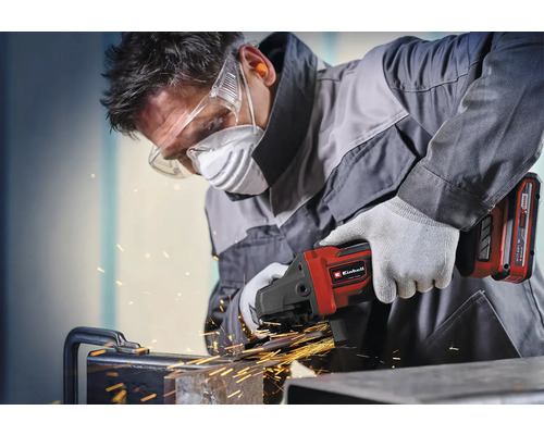 Remeselník pracuje s akumulátorovou uhlovou brúskou Einhell na kove s iskrami, má ochranné okuliare, respirátor, ochranu sluchu a rukavice.