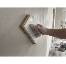 Ruka používajúca špongiové hladidlo na čerstvú omietku na stene.