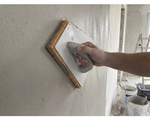 Ruka používajúca špongiové hladidlo na čerstvú omietku na stene.