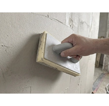 Ruka používa hubové hladidlo 28 krát 14 centimetrov na vyhladzovanie čerstvej omietky na stene.