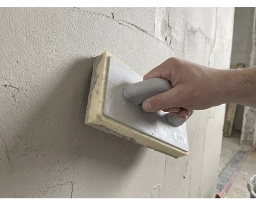 Ruka používa hubové hladidlo 28 krát 14 centimetrov na vyhladzovanie čerstvej omietky na stene.