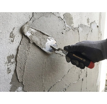 Ruka v pracovnej rukavici nanáša maltu na stenu pomocou murárskej lyžice Maurerlob.