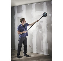 Muž brúsi sadrokartónovú stenu pomocou brúsky na sadrokartón s teleskopickou tyčou.