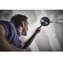 Muž brúsi sadrokartónovú stenu teleskopickou brúskou.