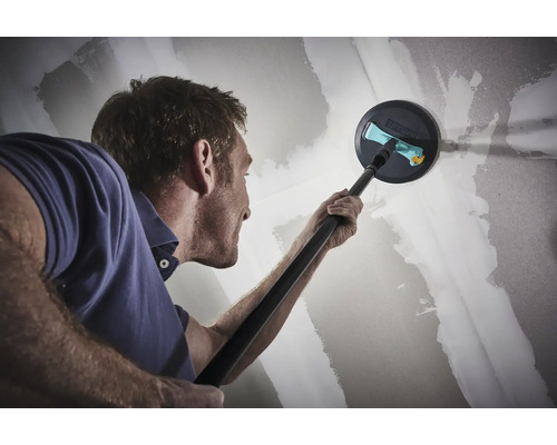 Muž brúsi sadrokartónovú stenu teleskopickou brúskou.