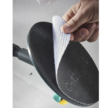 Ruka pripevňuje biely mriežkový brúsny kotúč na čierny okrúhly brúsny tanier brúsky na sadrokartón.