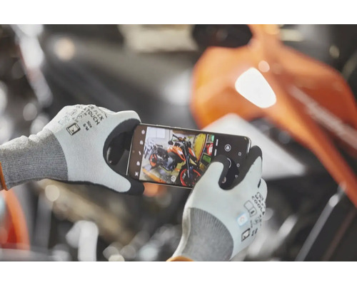 Osoba má na sebe pracovné rukavice s dotykovou funkciou a smartfónom fotografuje motocykel v dielni.