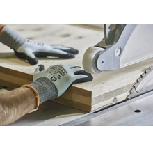 Ruky v pracovných rukaviciach vedú drevenú dosku na stolovej kotúčovej píle na presné opracovanie dreva.