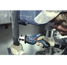 Remeselník reže tmavú rúru akumulátorovou chvostovou pílou Bosch Professional v pracovnom priestore so striebornými kovovými rúrami.