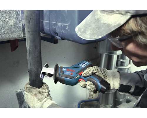 Remeselník reže tmavú rúru akumulátorovou chvostovou pílou Bosch Professional v pracovnom priestore so striebornými kovovými rúrami.