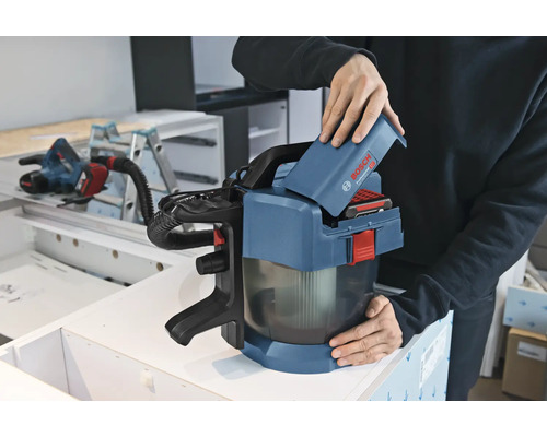 Osoba vkladá 18-voltový akumulátor do akumulátorového vysávača Bosch Professional GAS 18 Volt-1 v dielni.