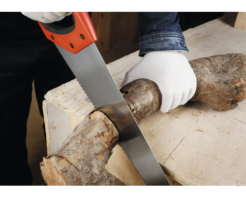 Osoba reže drevené poleno ručnou pílou na pracovnom stole.