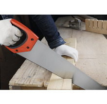 Osoba reže drevený hranol ručnou pílou na pracovnom stole v jasnej dielni.