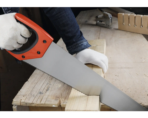 Osoba reže drevený hranol ručnou pílou na pracovnom stole v jasnej dielni.