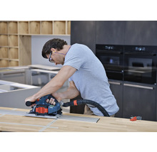 Muž používa kotúčovú pílu s vodiacou lištou a odsávaním prachu na drevenú pracovnú dosku v kuchyni.