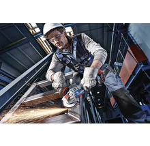 Remeselník v ochrannom odeve opracováva oceľovú konštrukciu akumulátorovou uhlovou brúskou, od ktorej lietajú iskry.