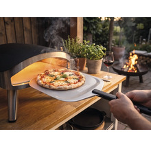 Čerstvo upečená pizza sa vyberá z prenosnej pece na pizzu na drevenom stole v záhrade pomocou lopaty na pizzu s Tenneker Logo.