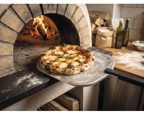 Čerstvo upečená pizza na lopate na pizzu s Tenneker Logo pred horiacou kamennou pecou v rustikálnej kuchyni.