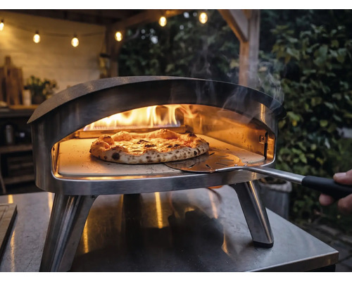 Vonkajšia nerezová pec na pizzu s horiacimi plameňmi a pizzou na pizzovom kameni, s ktorou sa manipuluje pomocou lopaty na pizzu.