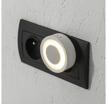 Okrúhle biele nočné LED svetlo so senzorom do zásuvky, zapojené do nástennej zásuvky.