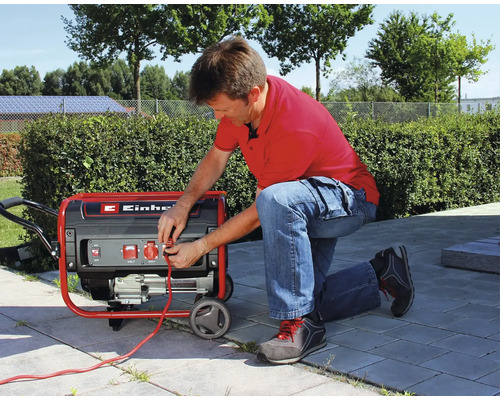 Muž kľačí na terase a zapája kábel do mobilnej elektrocentrály Einhell.