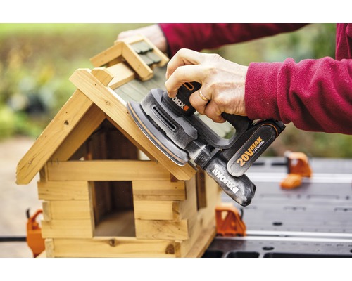 Osoba brúsi vtáčiu búdku excentrickou brúskou od spoločnosti Worx.