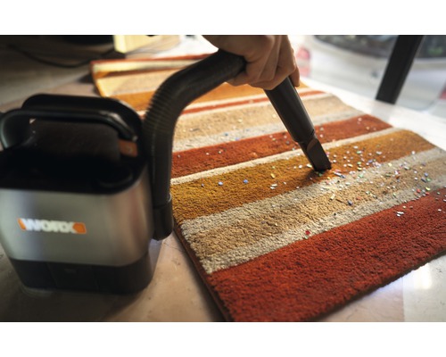 Akumulátorový vysávač sa používa na pruhovanom koberci na odstránenie malých častíc. Logo spoločnosti Worx.