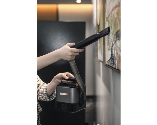 Osoba čistí obraz na stene pomocou prenosného vysávača Worx.