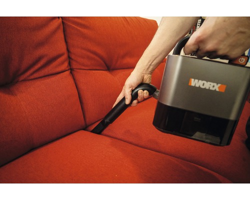 Osoba vysáva pohovku akumulátorovým vysávačom Worx