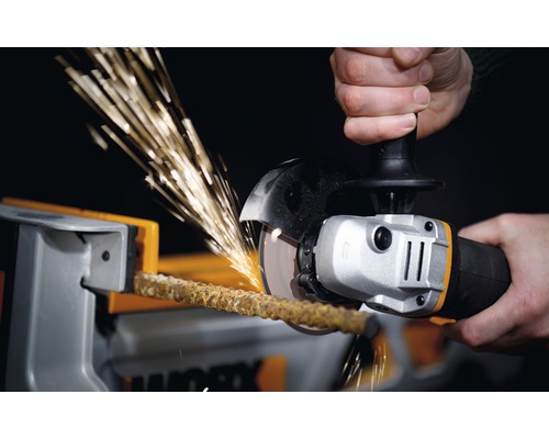 Osoba reže tyč vo zveráku uhlovou brúskou, čím vznikajú iskry.