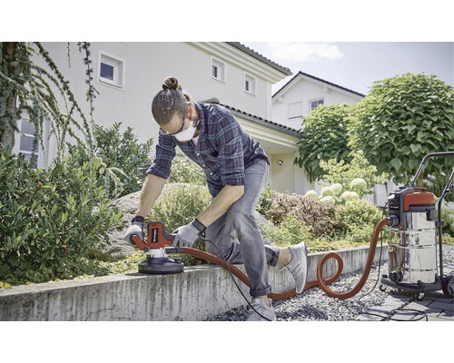 Muž brúsi betónový múr v záhrade pomocou brúsky na betón a vysávača.