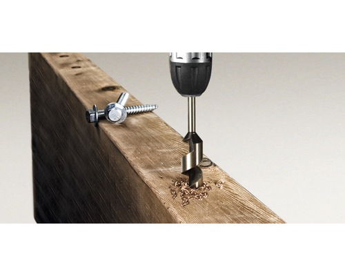 Vŕtačka vŕta otvor do drevenej dosky, vedľa ležia skrutky.