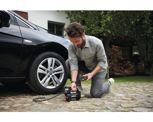 Muž hustí pneumatiku auta pomocou akumulátorového kompresora