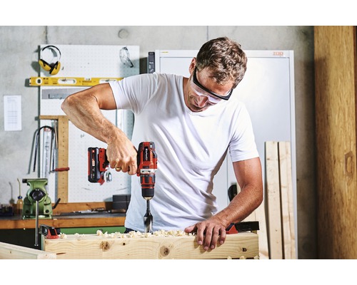 Muž vŕta vŕtačkou do drevenej dosky. Má ochranné okuliare.