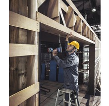 Remeselník vŕta akumulátorovým skrutkovačom otvor do drevenej konštrukcie.