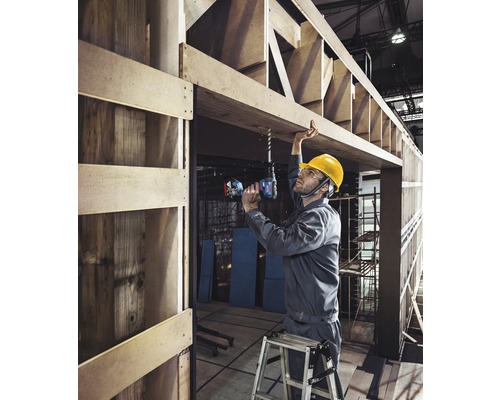 Remeselník vŕta akumulátorovým skrutkovačom otvor do drevenej konštrukcie.