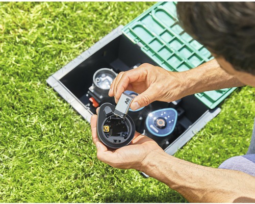 Muž vkladá batériu do zavlažovacieho počítača v šachte v trávniku