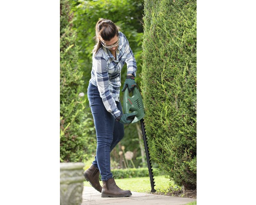 Žena strihá živý plot nožnicami na živý plot Bosch v záhrade.